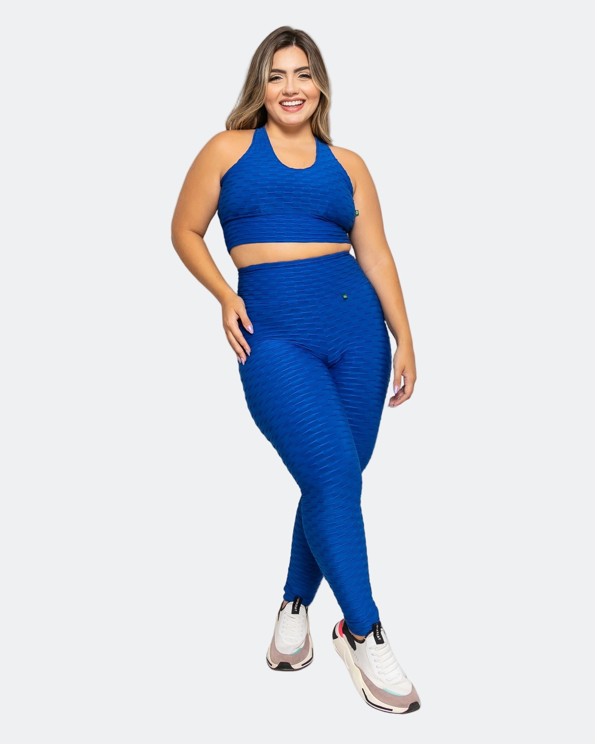 Woman wearing blue high-waisted brazilian butt lift leggings with a matching 3 in 1 active crop top and white sneakers
