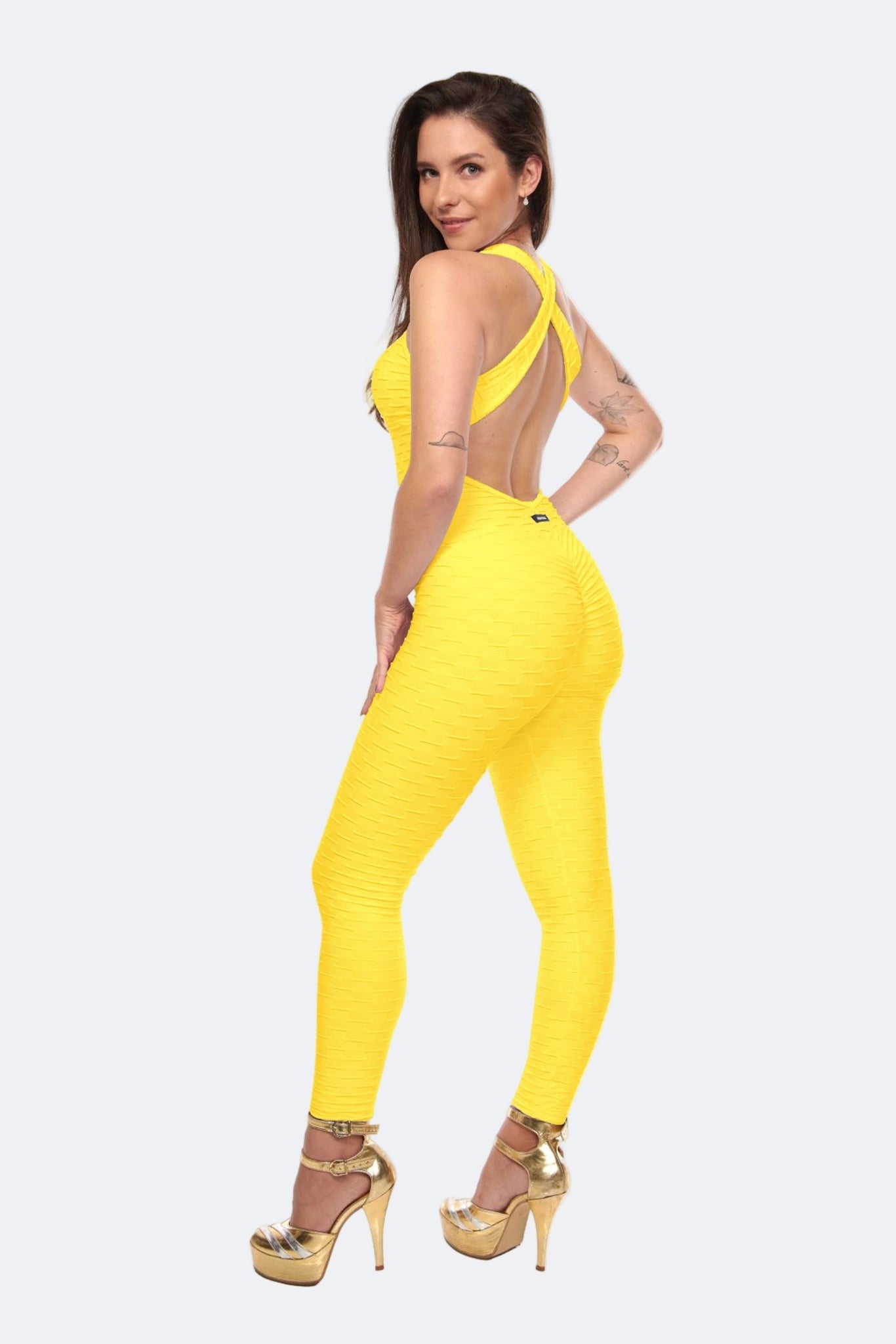 A woman posing in a yellow scrunch booty jumpsuit, which is designed to accentuate the figure.