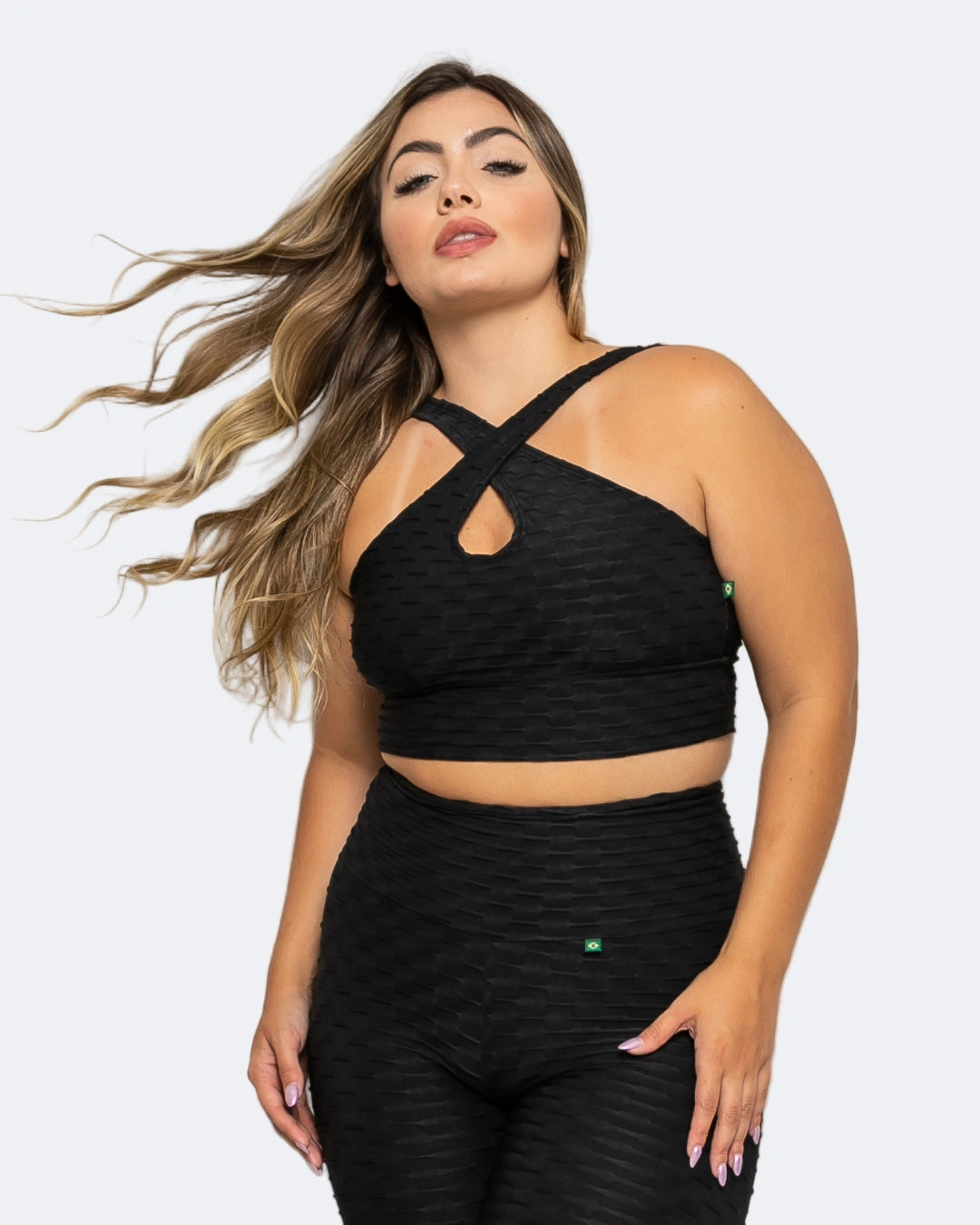 A woman wearing a black active sports bra with a textured fabric, featuring a halter neck design and crisscross straps.
