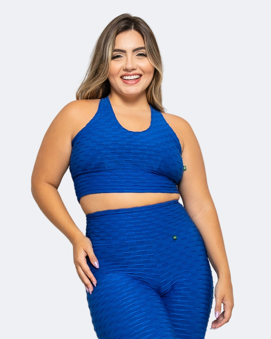 A woman wearing a blue sports bra with a textured fabric, featuring a halter neck and crisscross strap design.
