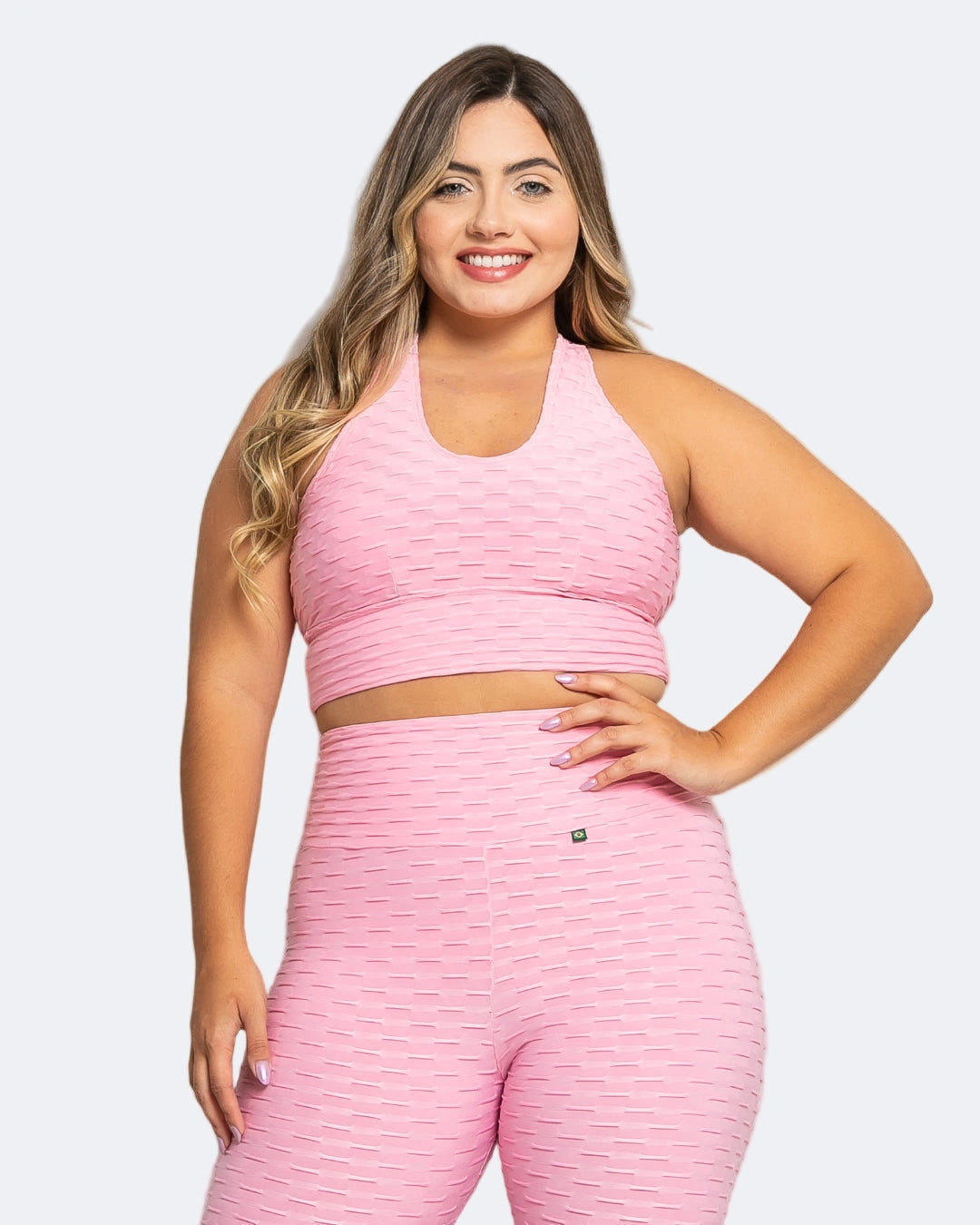 A woman wearing a pink sports bra and matching leggings, standing against a grey background.