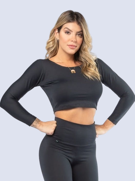 A model wearing a long sleeve black crop top and black leggings, standing with one hand on her hip.
