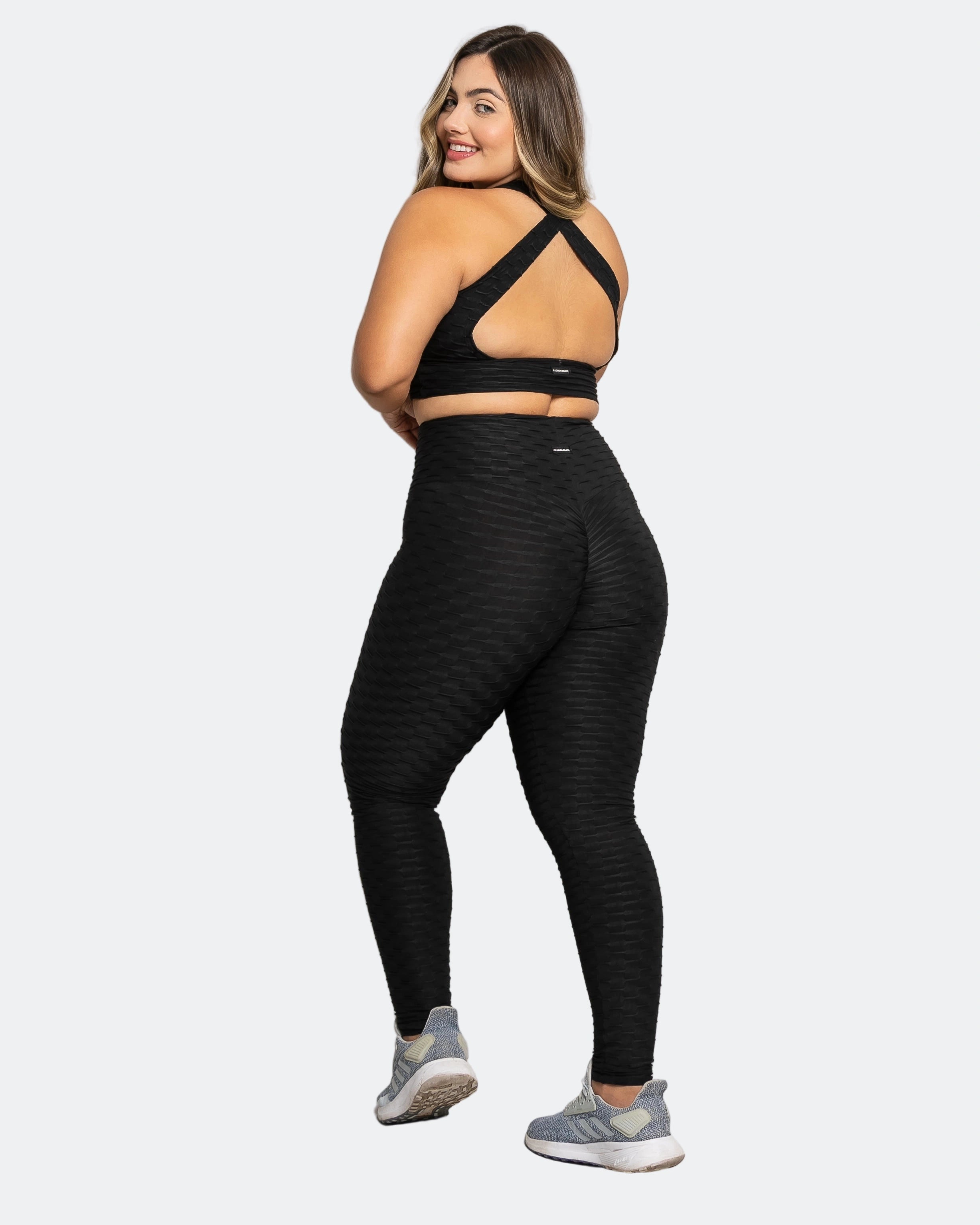 Woman wearing black athletic leggings and sports bra on a white background