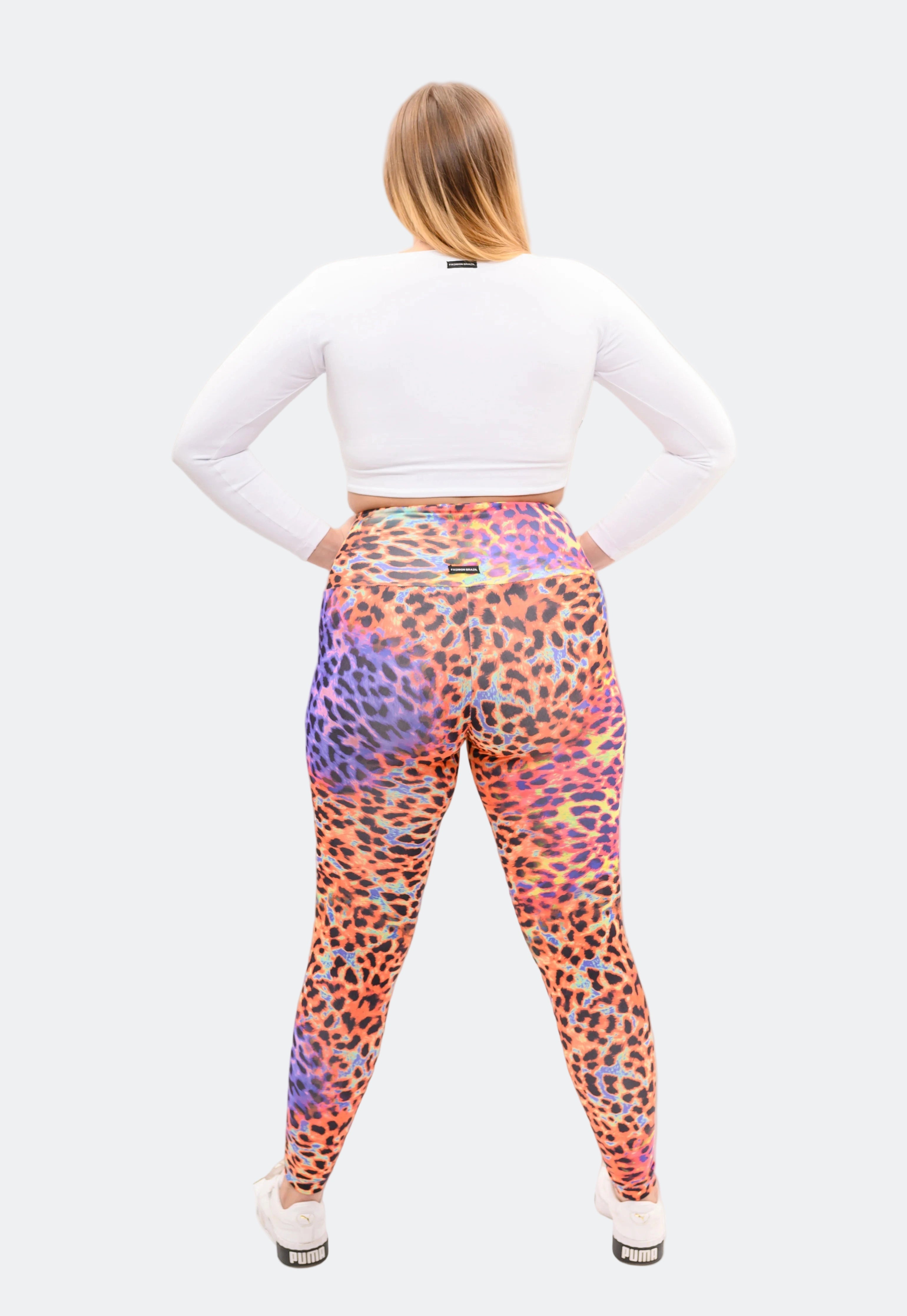 Person wearing colorful leopard print leggings with a white top on a light gray background