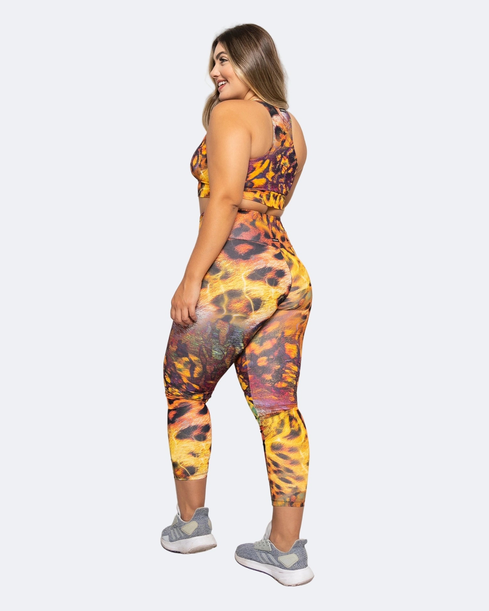 Woman wearing a colorful safari animal print 7/8 leggings and racerback sports bra on a white background