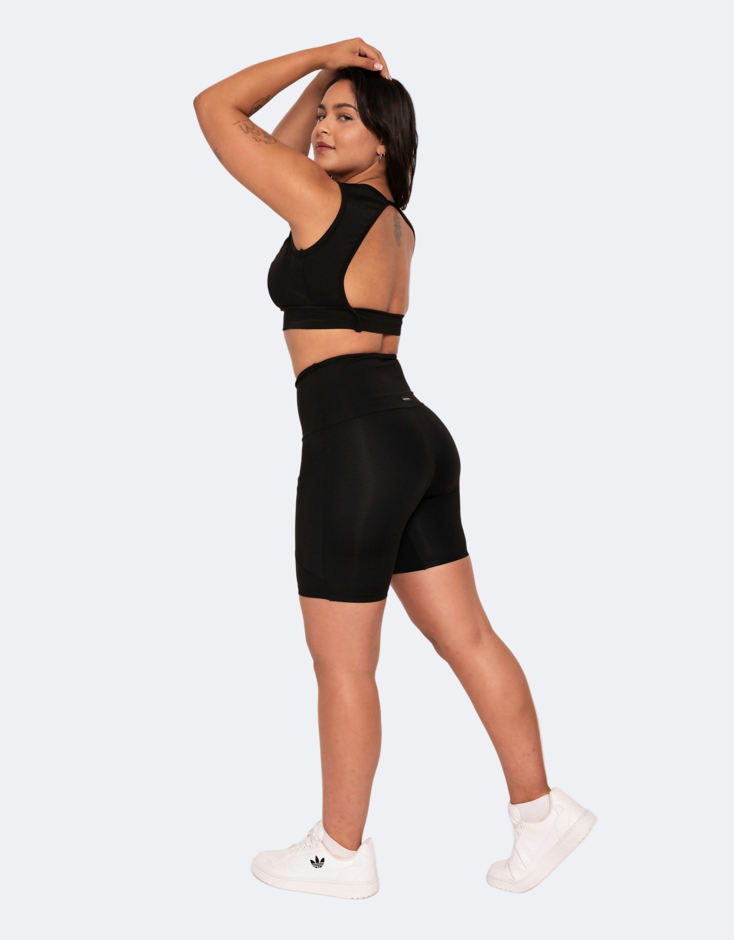 model is  wearing a black mid length high waisted shorts and black active crop top on a white background