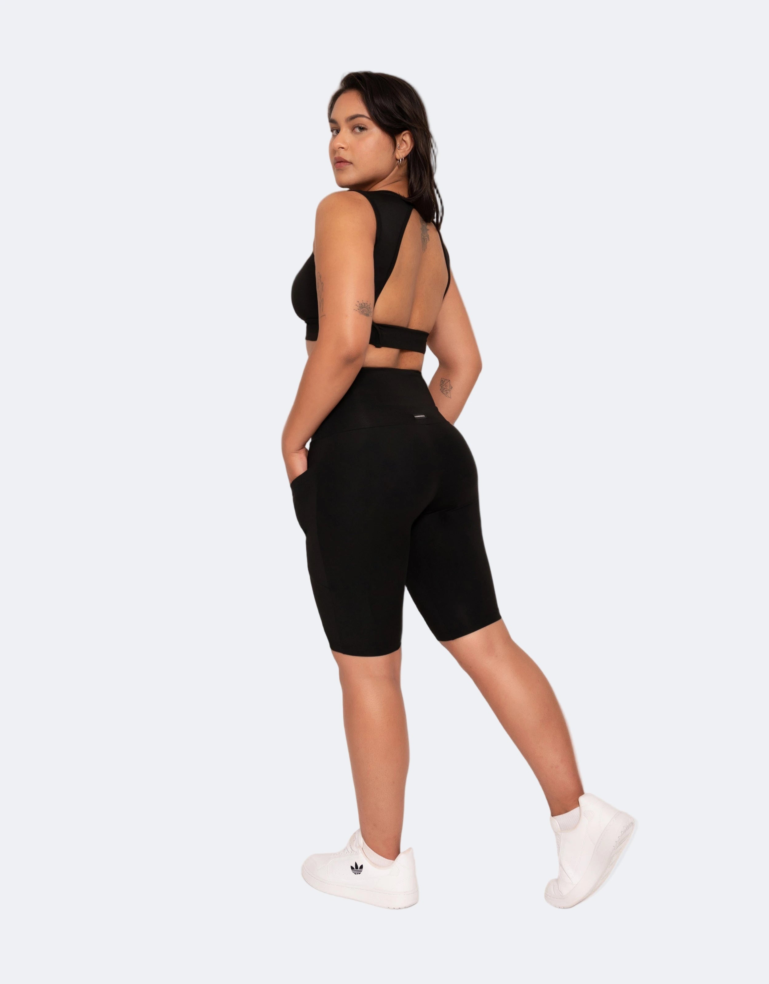 Side view of a person wearing a black bike shorts with pockets and a matching sports crop top with a white background
