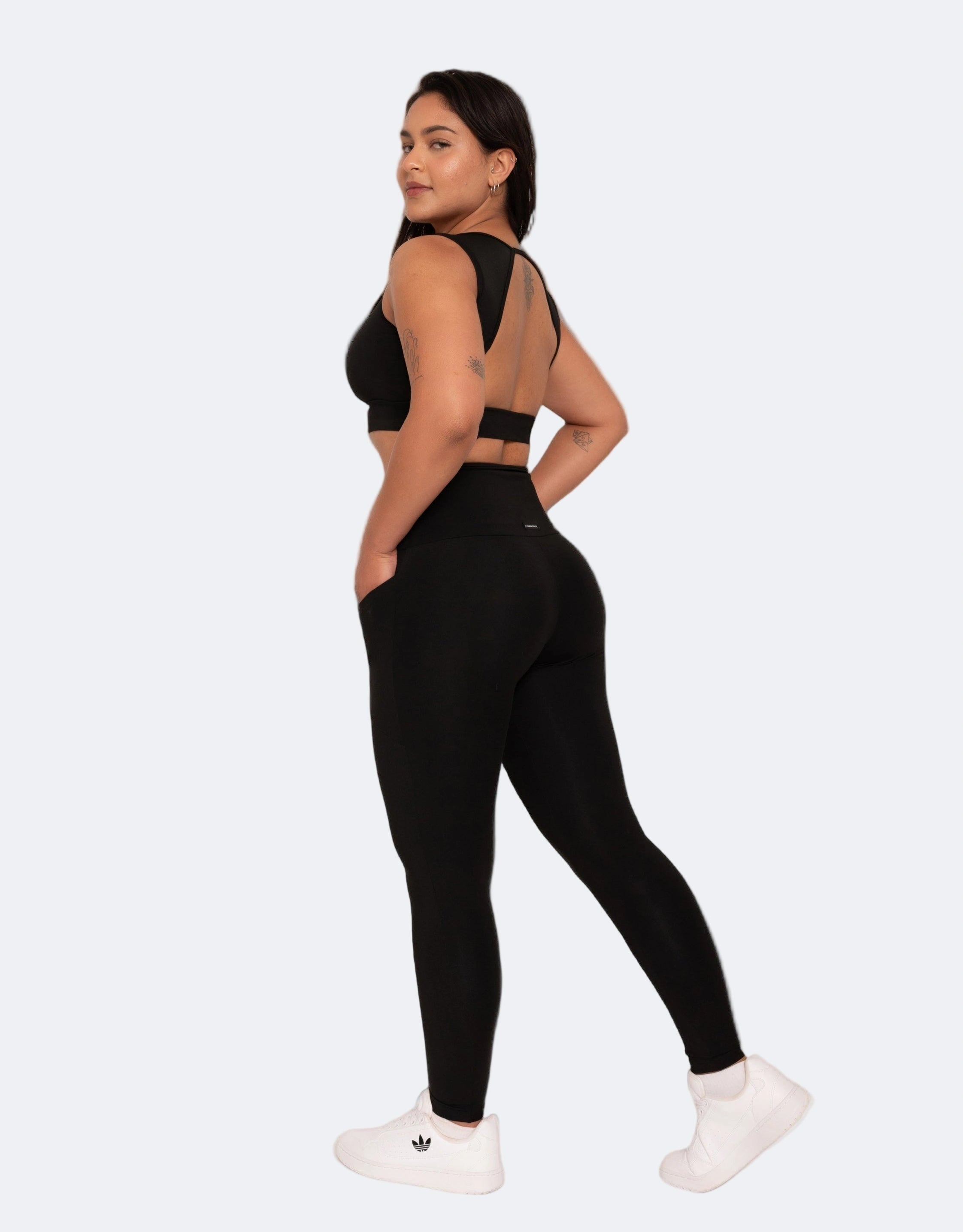 Woman wearing a black sports bra and leggings with white sneakers on a light gray background