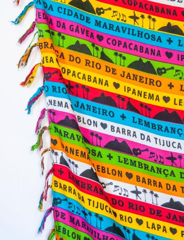 Close-up of Lembrança do Rio Fitinha Sarong showing the Bonfim wish ribbon print detail and multicolor fabric on a white background

