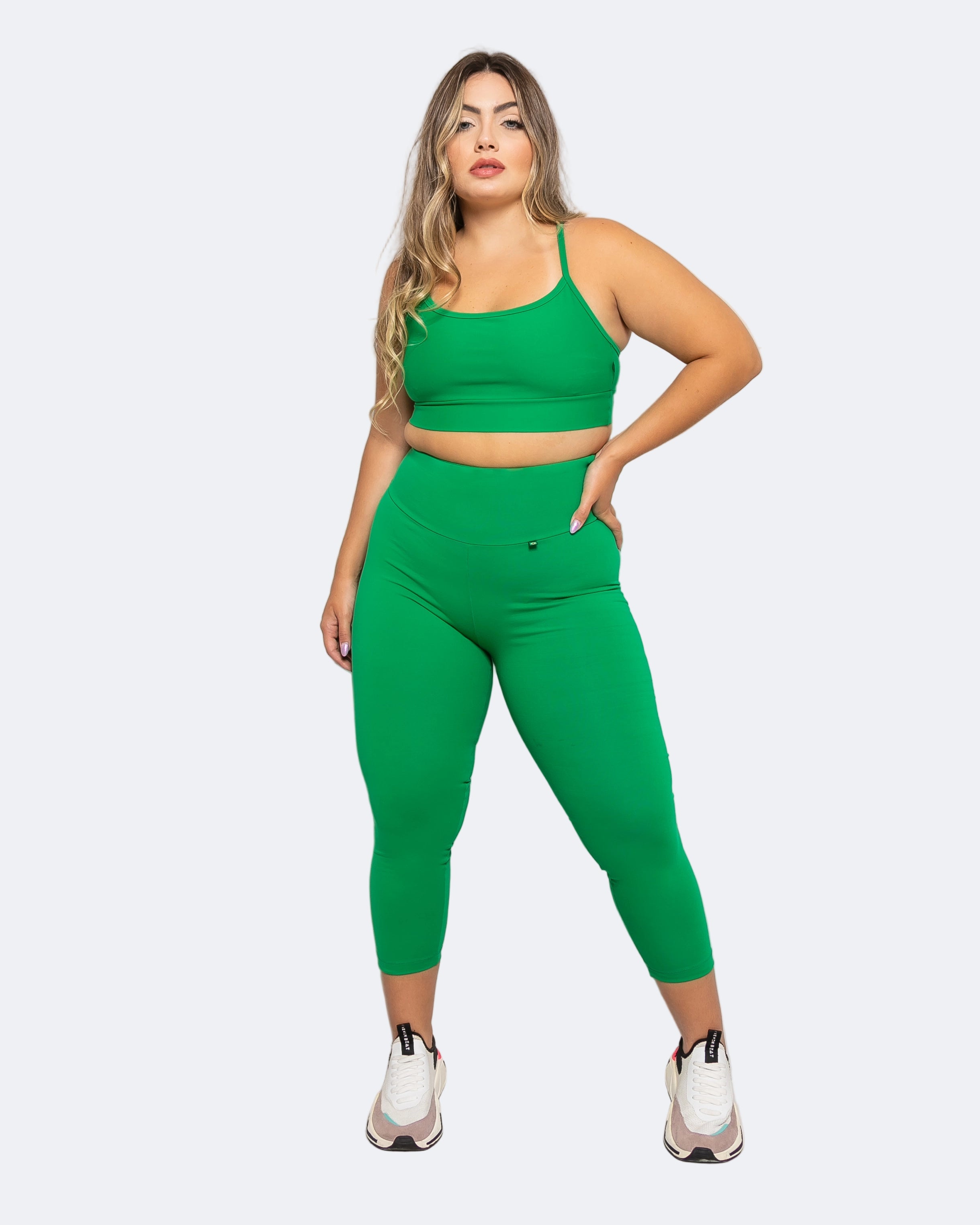 A model wearing a matching set of green high-waisted compressive leggings and sports bra, standing against a neutral background.