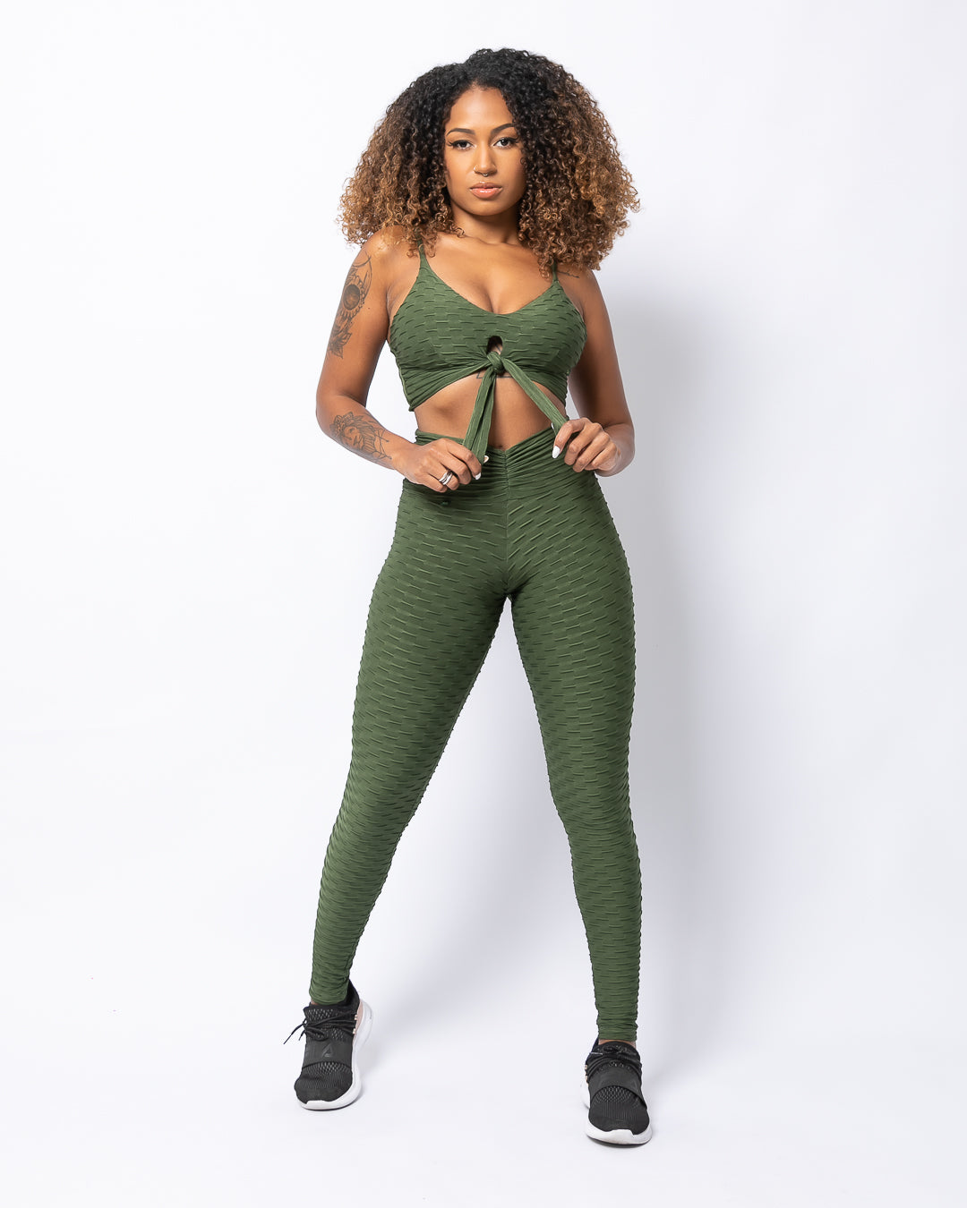 A model wearing a matching set of forest green V-waistband leggings and sports bra, posing against a plain background.